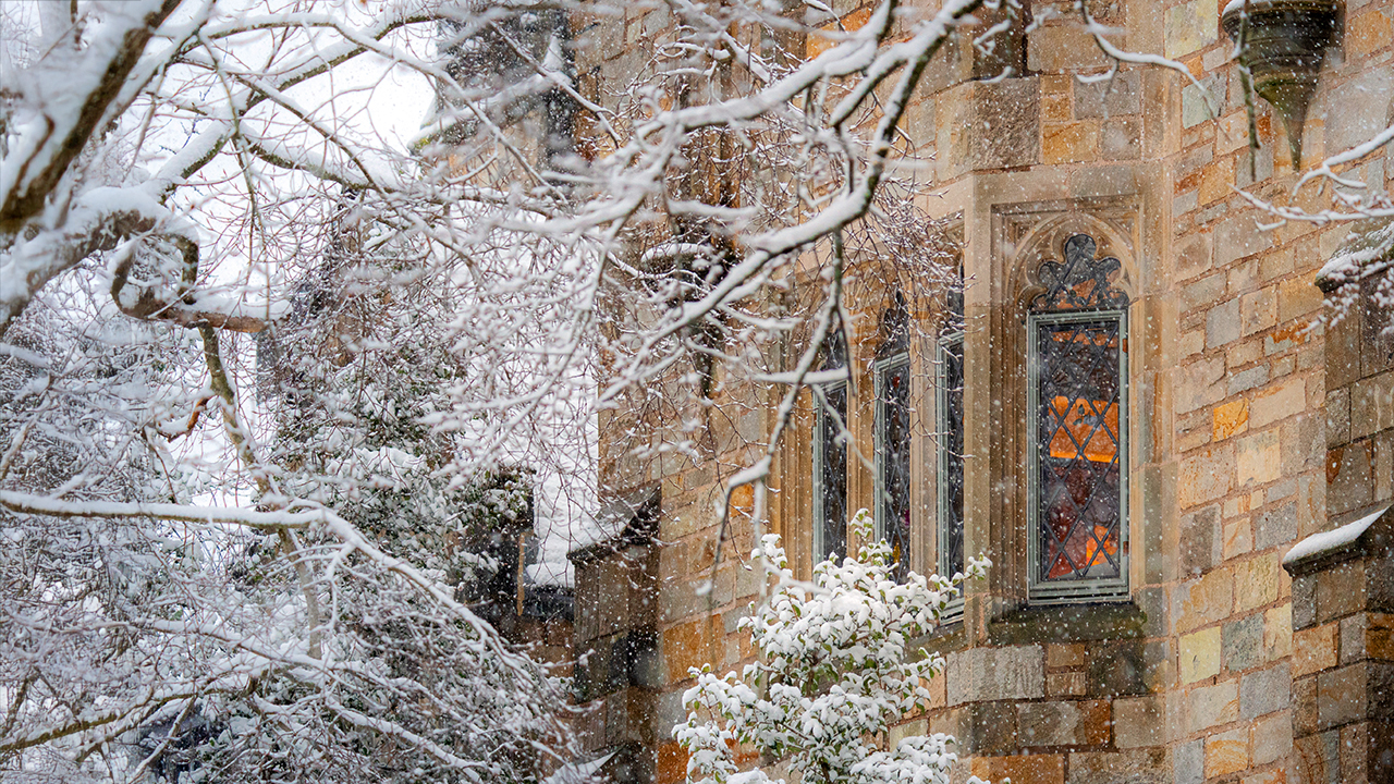 Snowy branches surrounding a stained-glass window of a Yale building